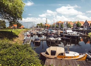 Un port de plaisance avec des bateaux amarrés, une jetée en bois et, au fond, des bâtiments aux toits rouges.