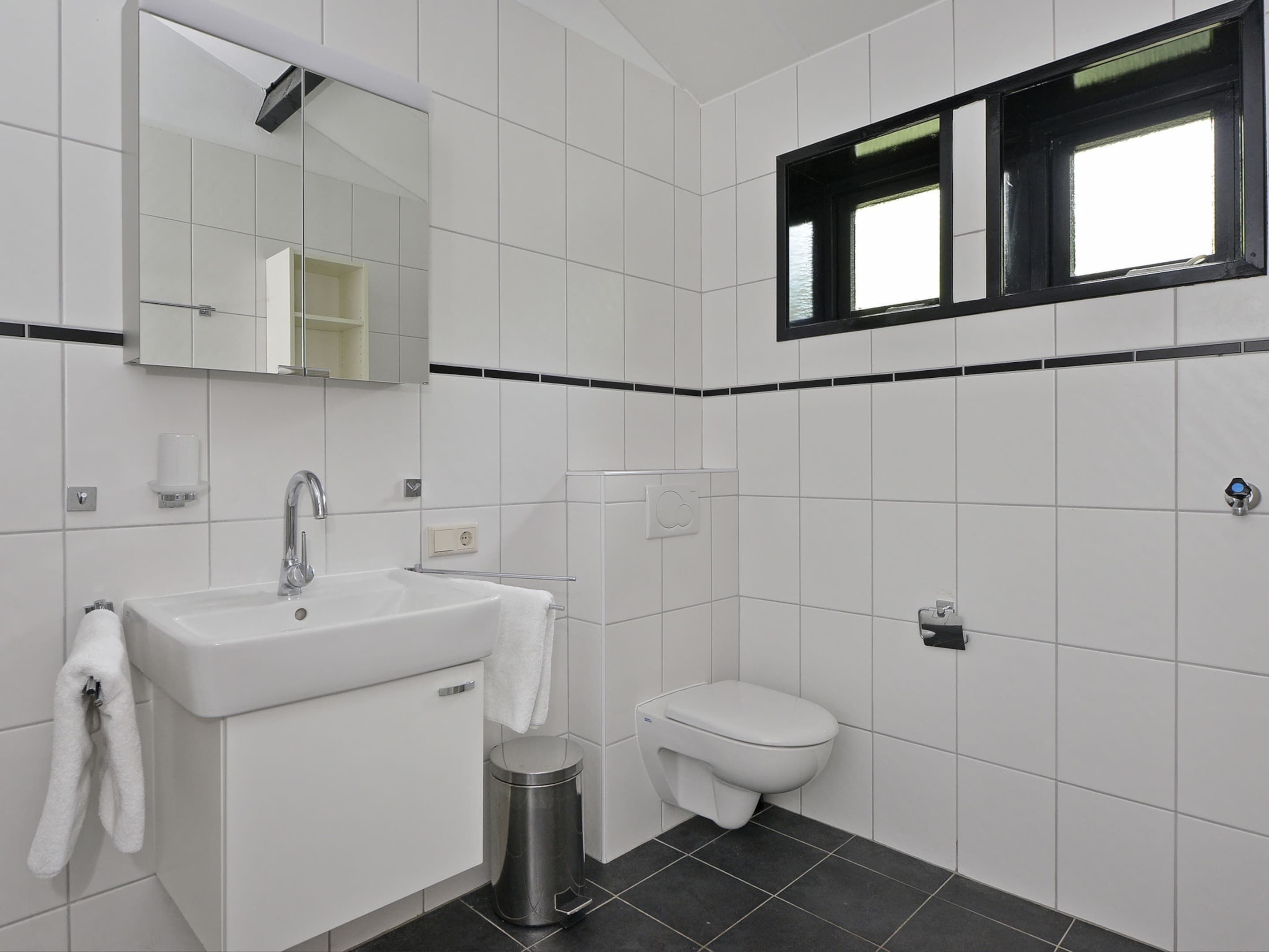 A modern bathroom with a white sink, mirror, and toilet.