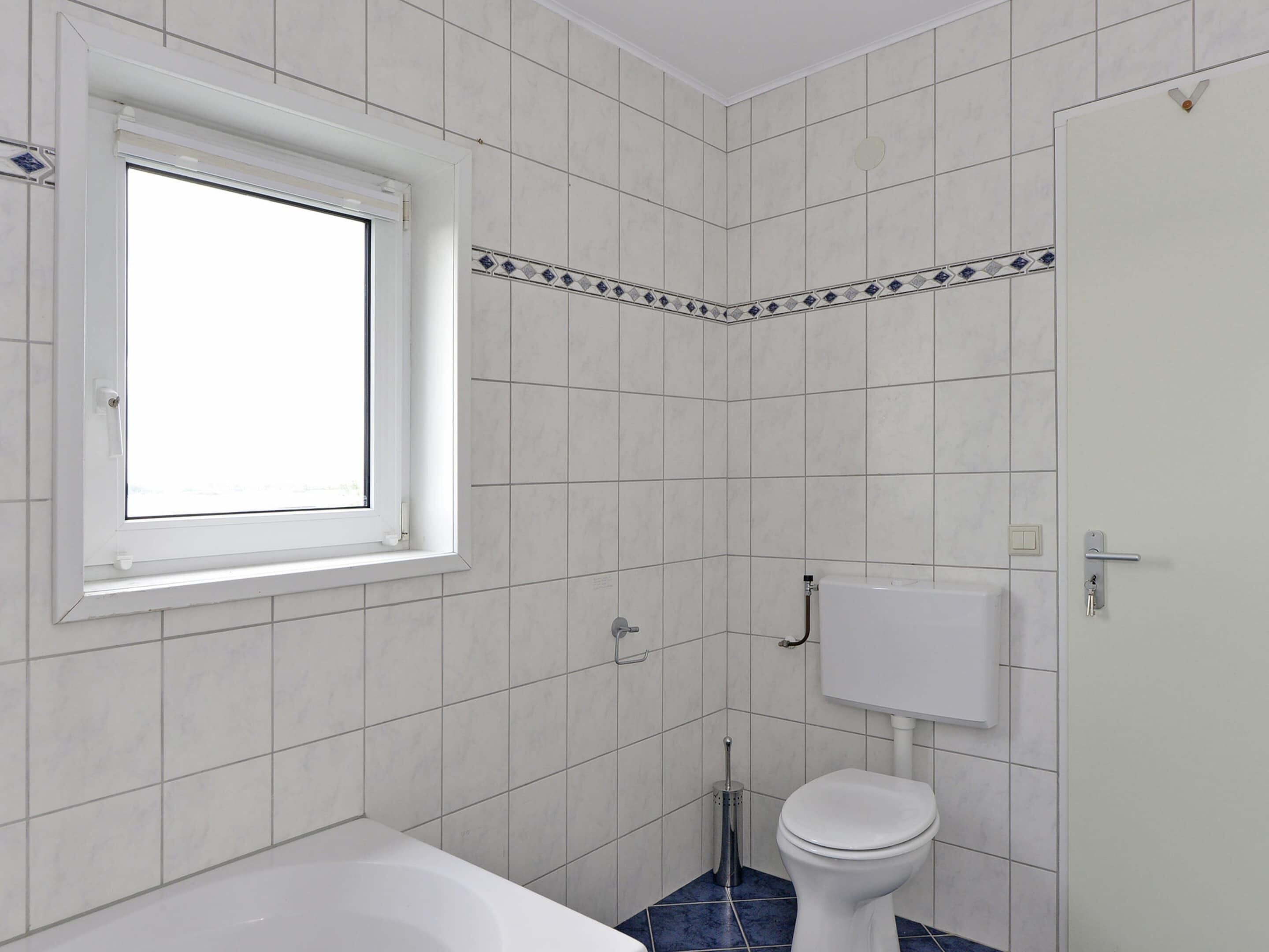 A bathroom with white tiles, a window, a bathtub, a toilet, and a shower.