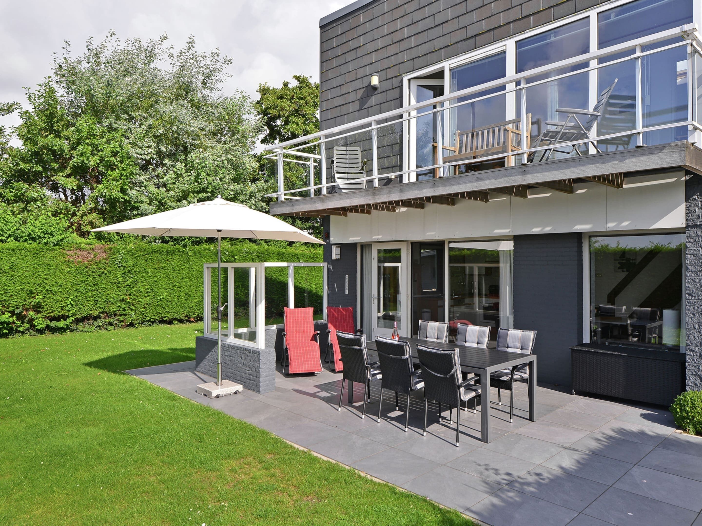 Une maison moderne dotée d’un patio comprenant une table et des chaises, un espace salon couvert et un grand parasol.