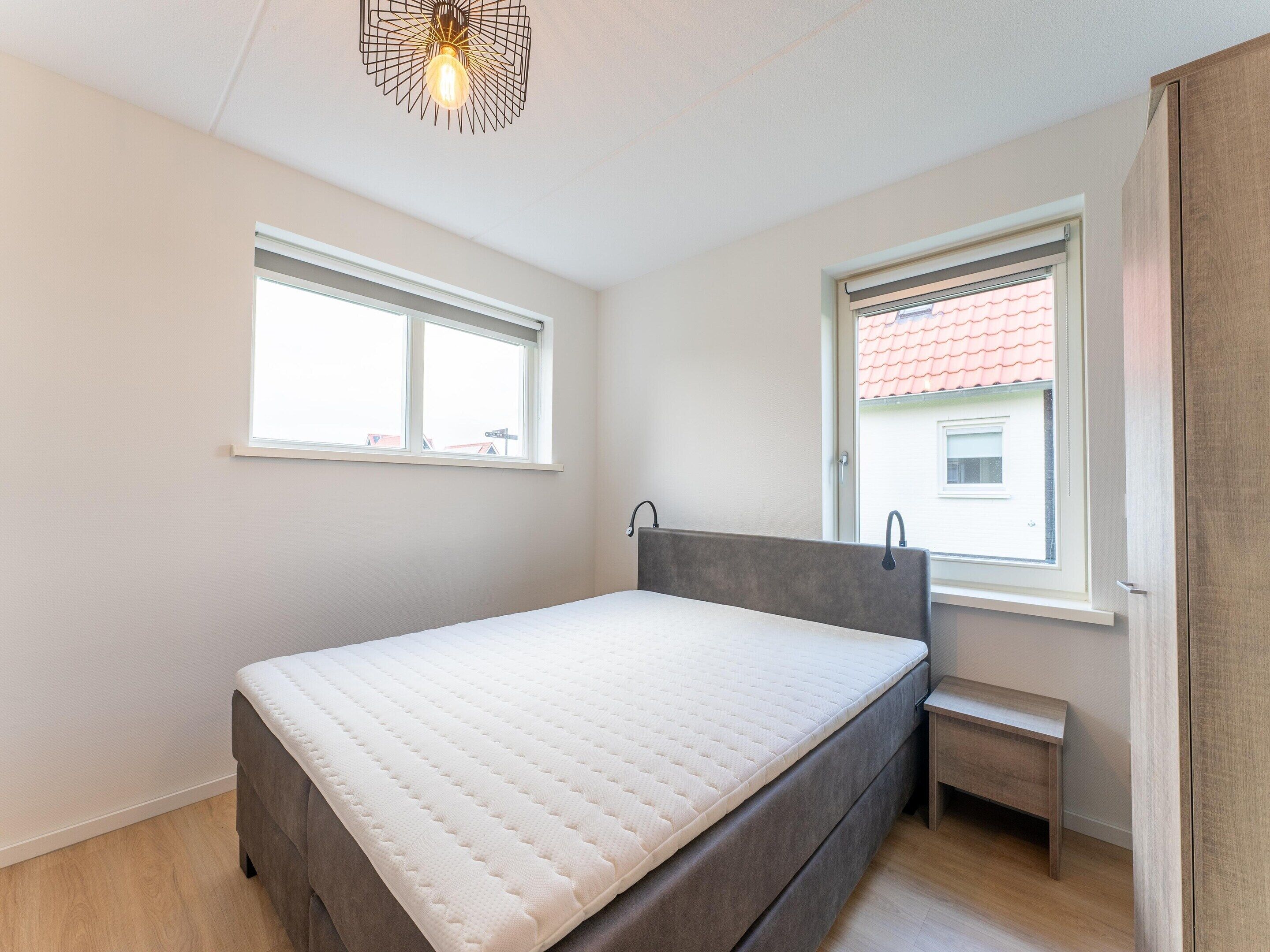 Una camera da letto con un letto, due finestre, una panca e una lampada a sospensione.