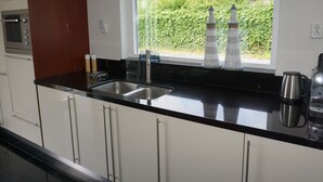 Een moderne keuken met een zwart aanrecht, een roestvrijstalen spoelbak en een raam met uitzicht op groen.