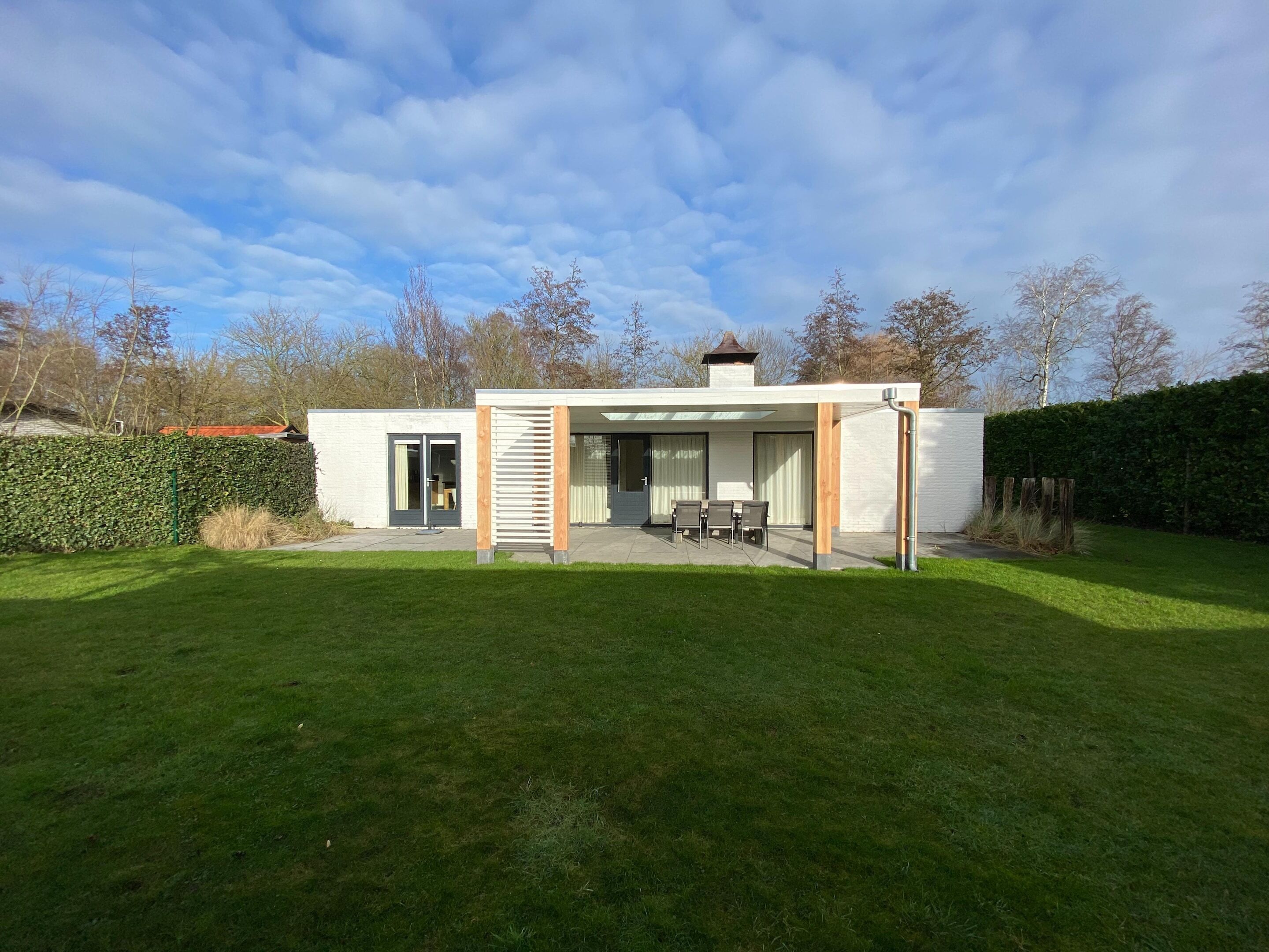 A modern house with a covered patio, a small garden, and a clear sky.