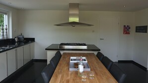 Een moderne keuken met een centraal eiland, zwarte aanstaltinten en een roestvrijstalen afzuigkap.