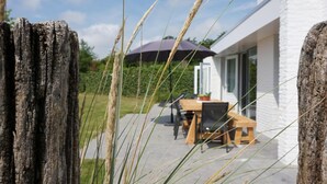 Een modern huis met een patio voorzien van een tafel en stoelen, omgeven door hoge grassen.