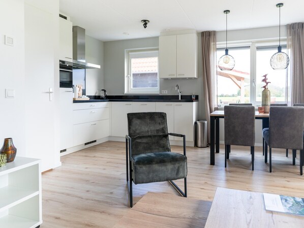 A modern kitchen with white cabinets, a black countertop, and a dining area with grey chairs and a table.