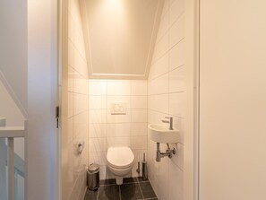 Um banheiro pequeno e moderno com azulejos brancos, vaso sanitário, pia e lixeira.