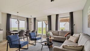 A modern living room with a sofa, chairs, a coffee table, and a dining area with a table and chairs. - Vacation Home Zeeland by Oosterschelde Park (Scherpenisse)