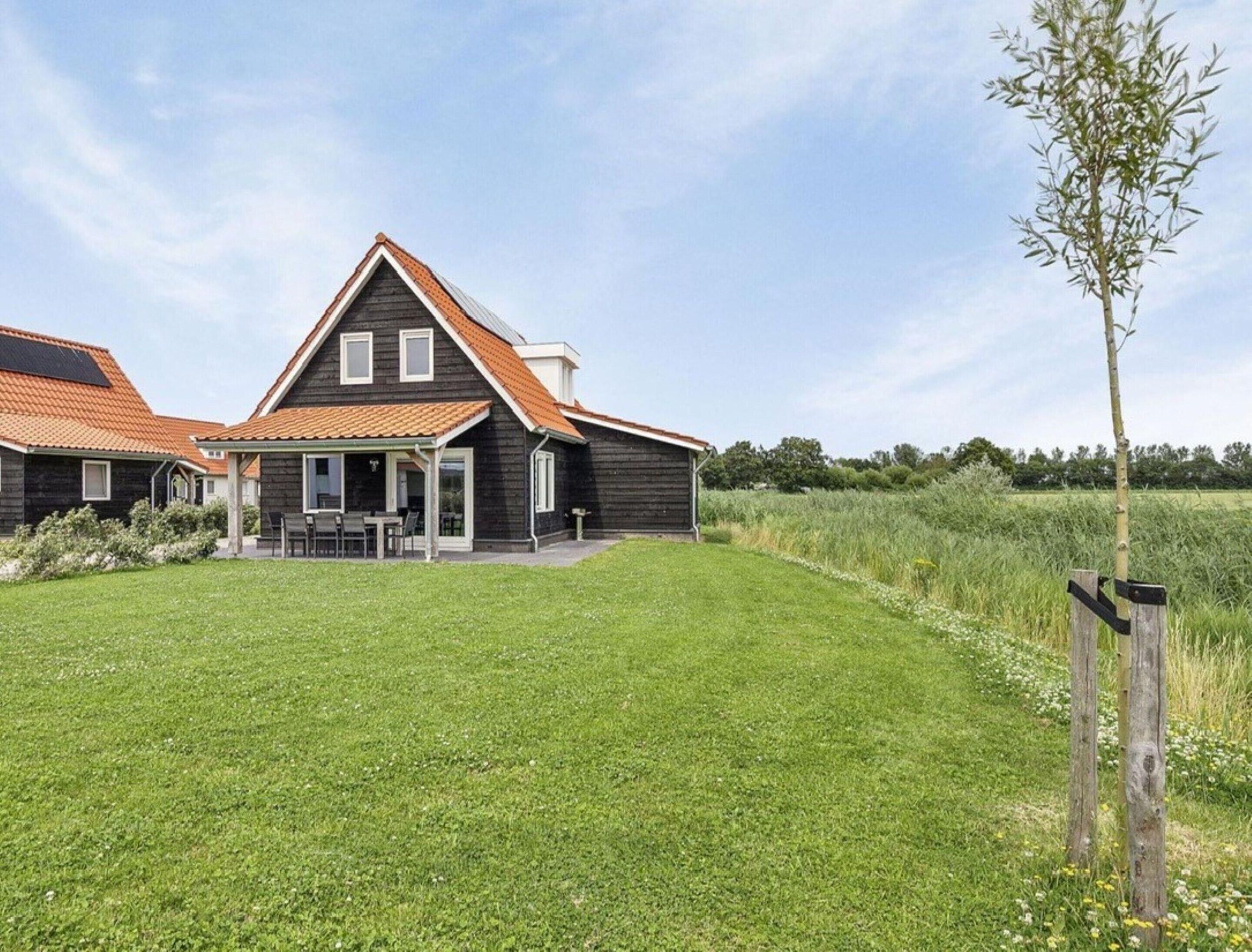 Een modern huis met twee verdiepingen, een schuin dak, een overdekt terras en een verzorgd gazon.