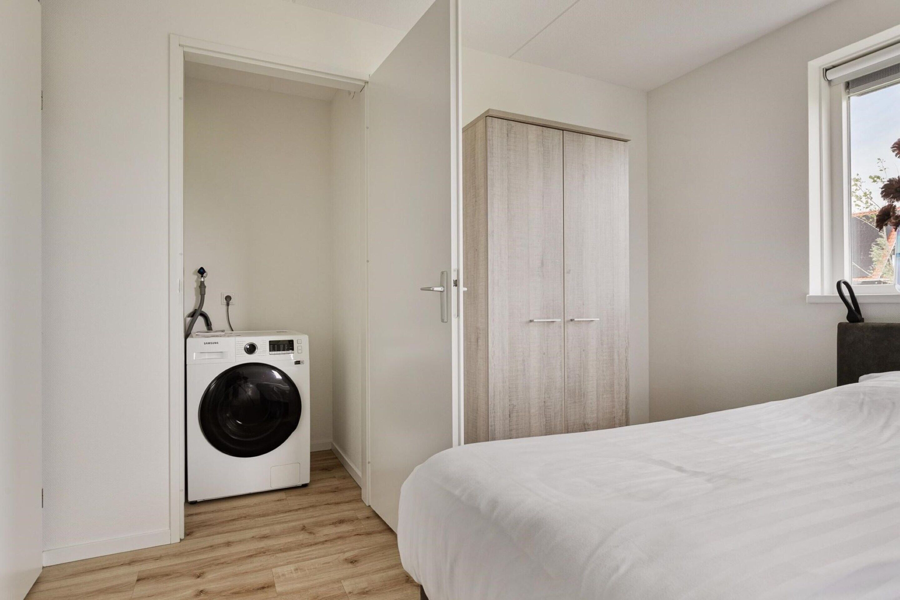 A bedroom with a bed, a washing machine, and a wardrobe.
