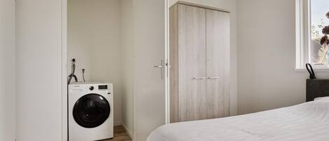 A bedroom with a bed, a washing machine, and a wardrobe.