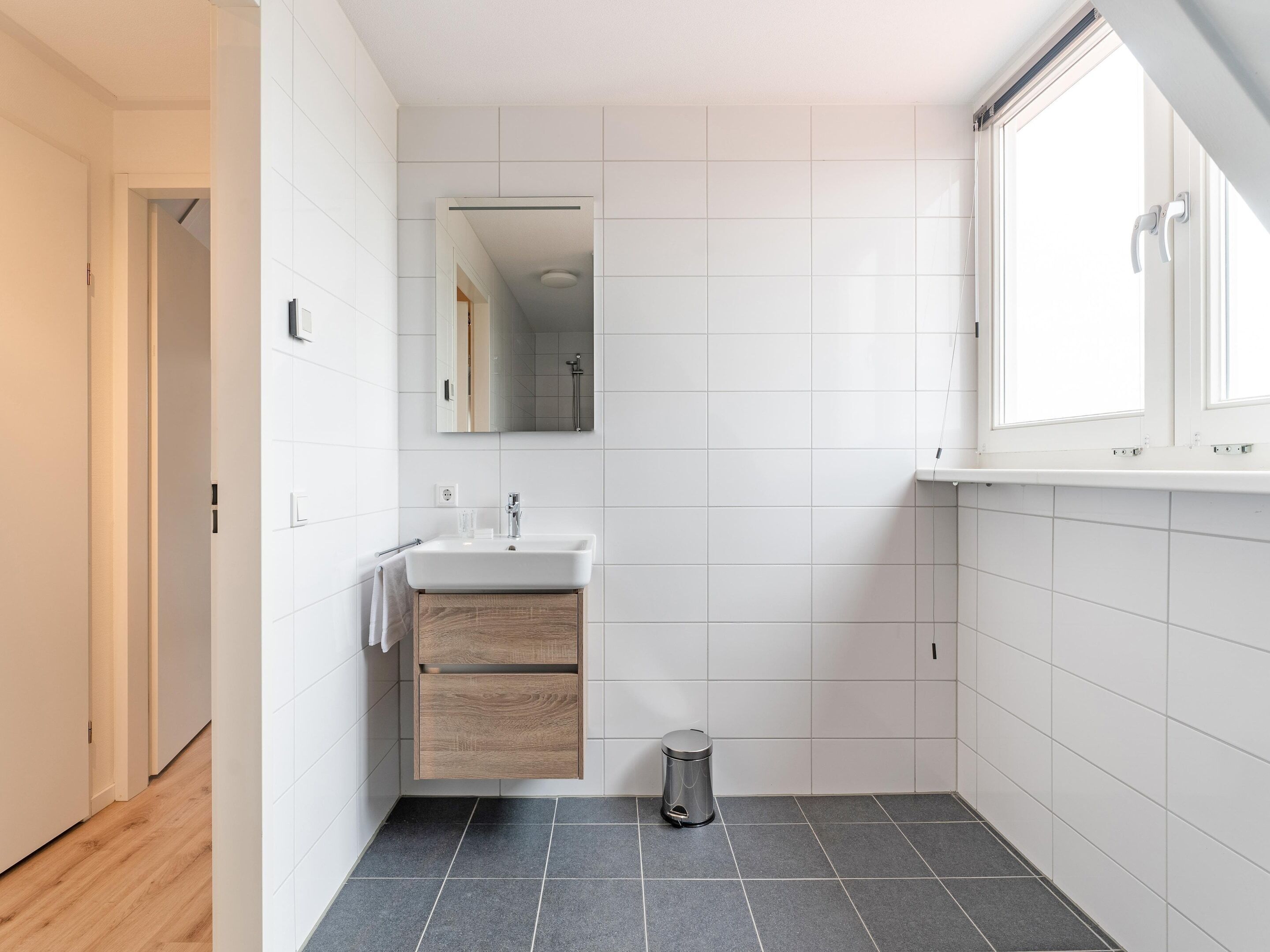 Un bagno moderno con lavandino bianco, specchio e pareti rivestite di piastrelle.