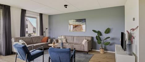 A modern living room with a grey sofa, blue chairs, a small table, and a large window.