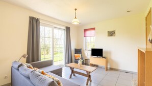 Una sala de estar con un sofá, una mesa de centro, un televisor y una ventana con cortinas.