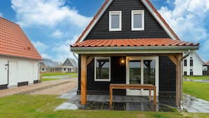 A black house with a tiled roof, a small porch, and a table. - Modern Holiday Home by the sea With Sauna (Scherpenisse)