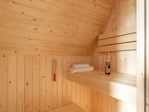 Un sauna en bois, avec une bouteille de champagne, des serviettes et un thermomètre pour sauna.
