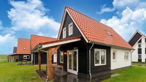 A modern house with a black and white exterior, a red-tiled roof, and a covered patio area. - Modern Holiday Home by the sea With Sauna (Scherpenisse)