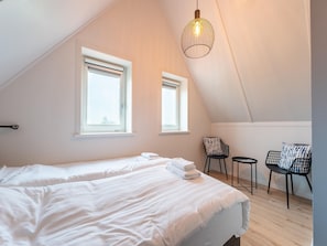 A bedroom with two beds, a hanging light fixture, two windows, and a chair.