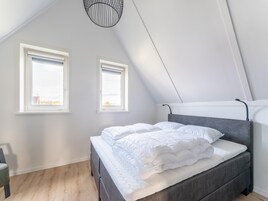 Un dormitorio con una cama, dos ventanas, una lámpara colgante y vistas al exterior.