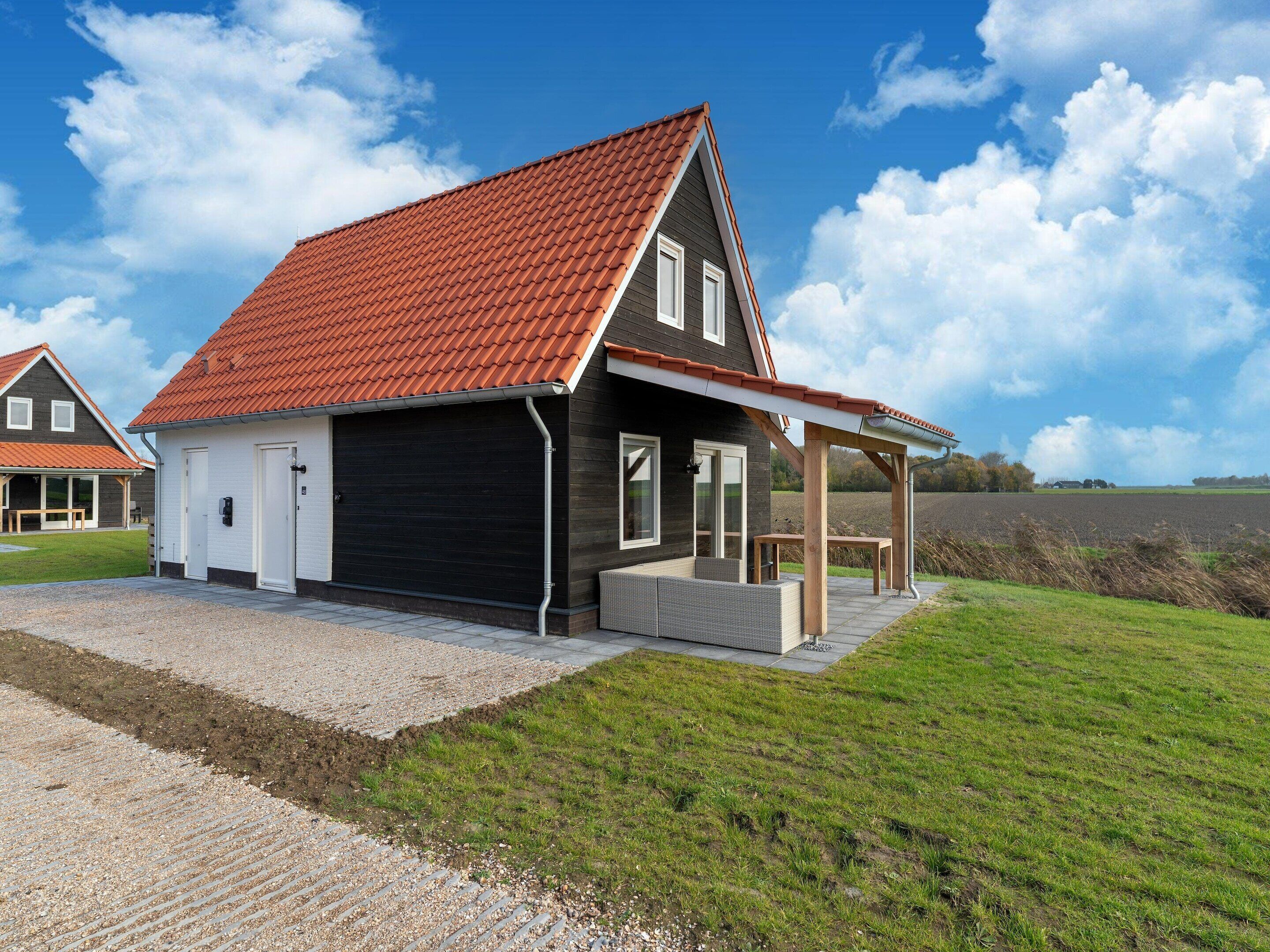 Een modern huis met een rode dakbedekking, een overdekte veranda en een grindpad.