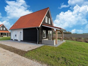 Et moderne hus med rødt tegltag, en overdækket veranda og en grusbelagt indkørsel.