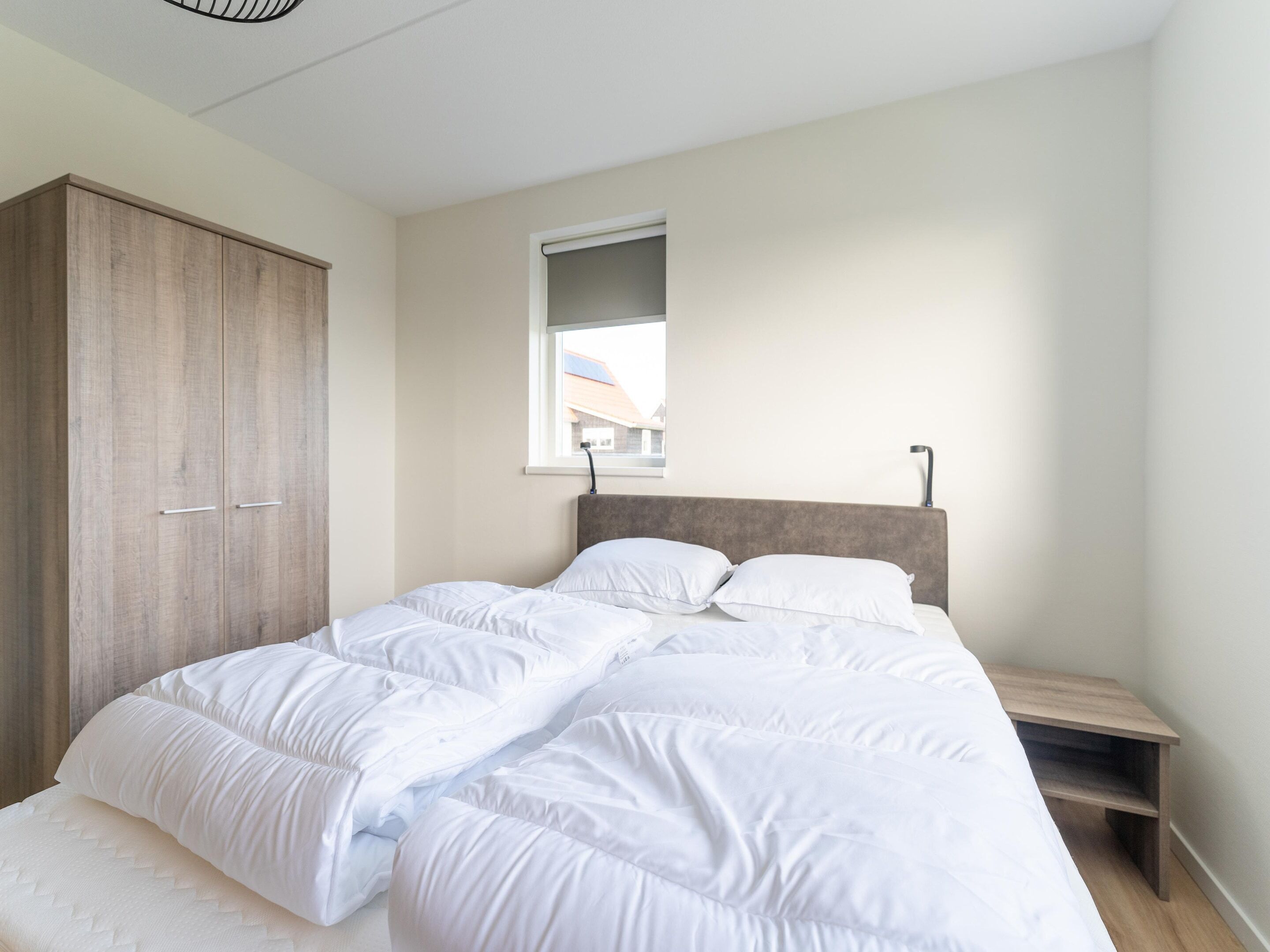 A bedroom with a bed, a wardrobe, a window, and a bedside table.