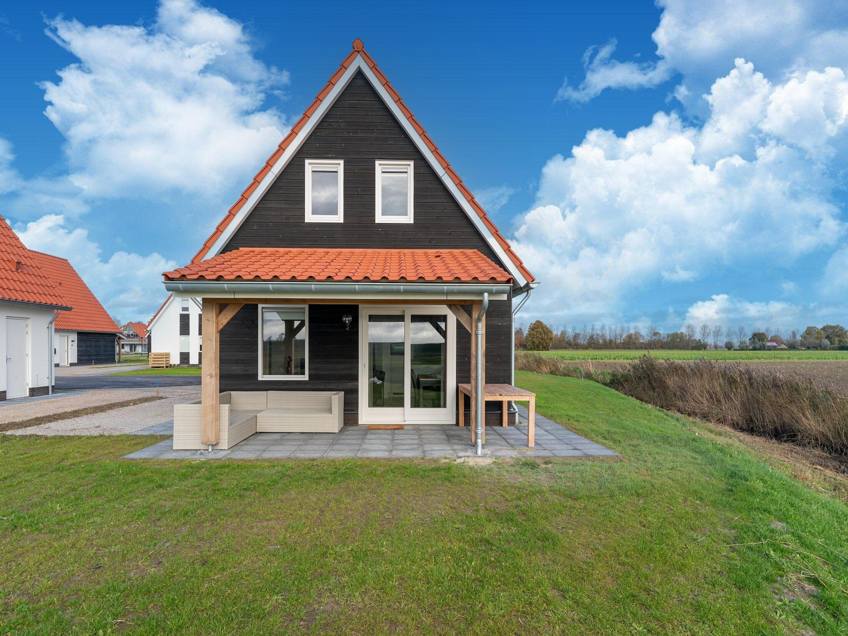 A single-story house with a dark facade, a red-tiled roof, and a small porch with a table and chairs.