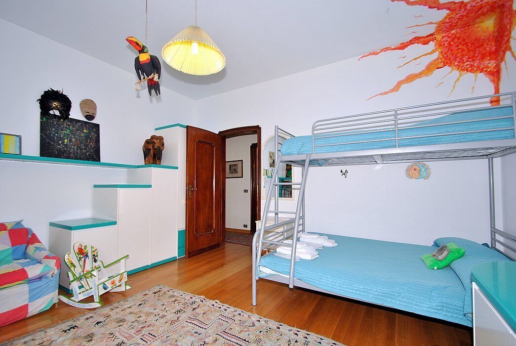 A room with a bunk bed, a desk, a chair, and a hanging lamp.