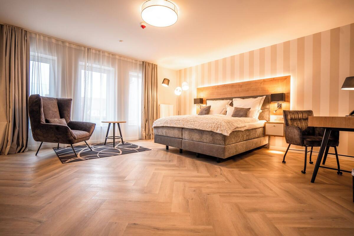 A hotel room with a large bed, a desk with a chair, a sofa, and a chair.