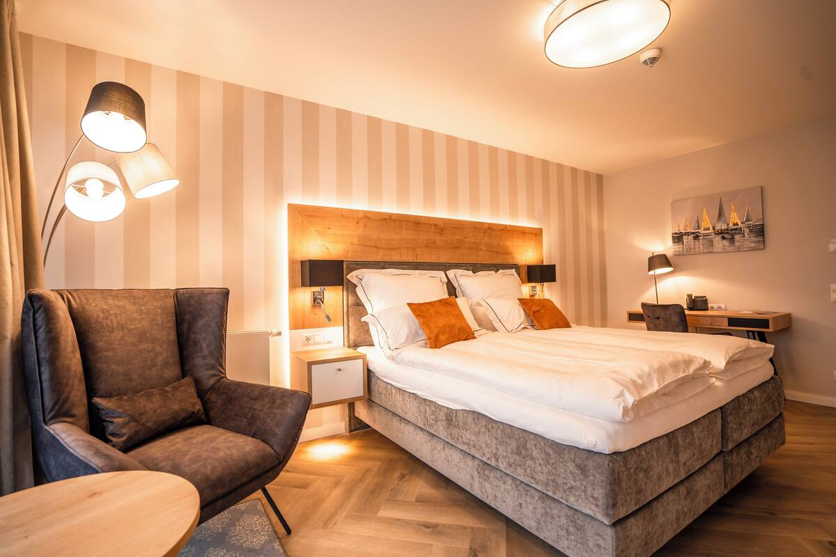 A modern bedroom with a large bed, a leather armchair, a wooden nightstand, and a desk with a chair.