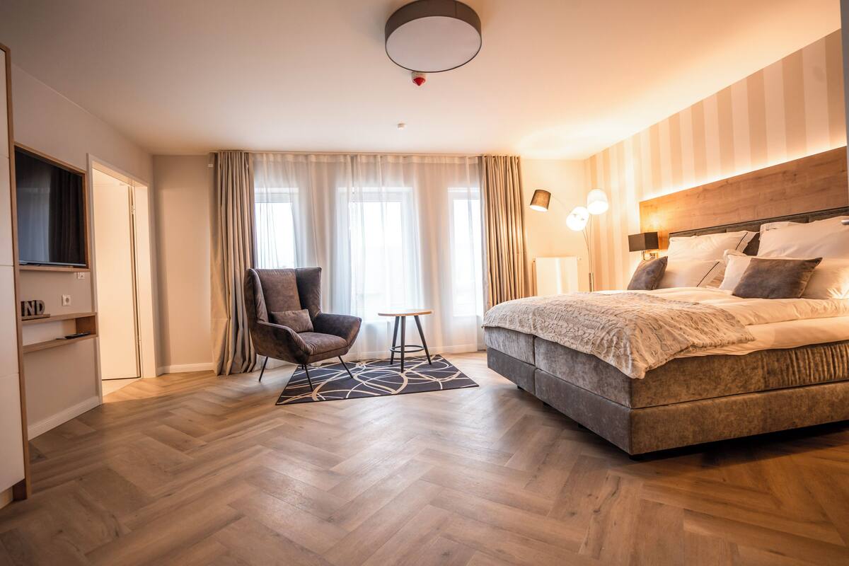 A modern hotel room with a large bed, a chair, a small table, and a TV.