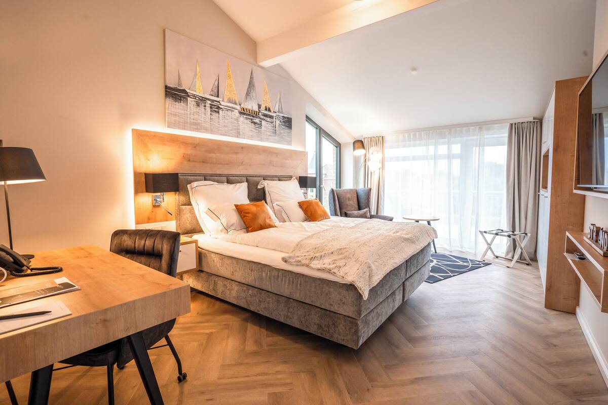 A modern hotel room with a large bed, a desk, and a view of the city.