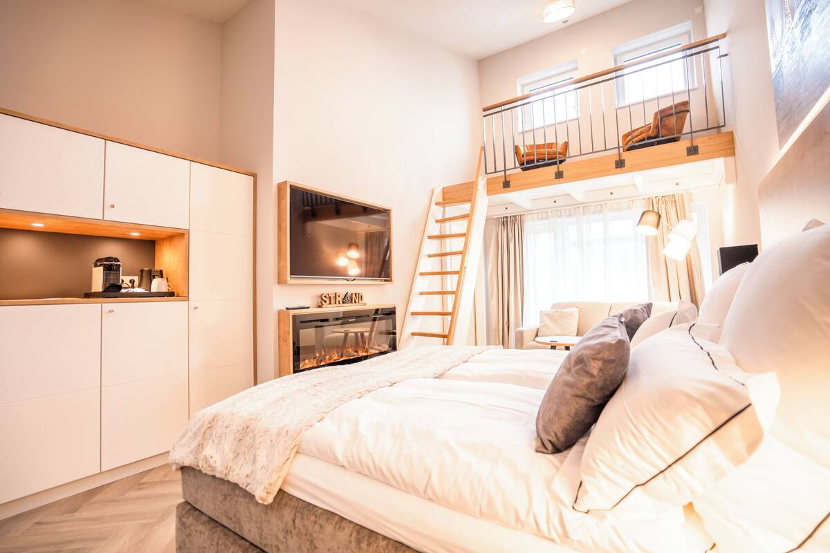 A modern bedroom with a bunk bed, a fireplace, a TV, and a balcony.