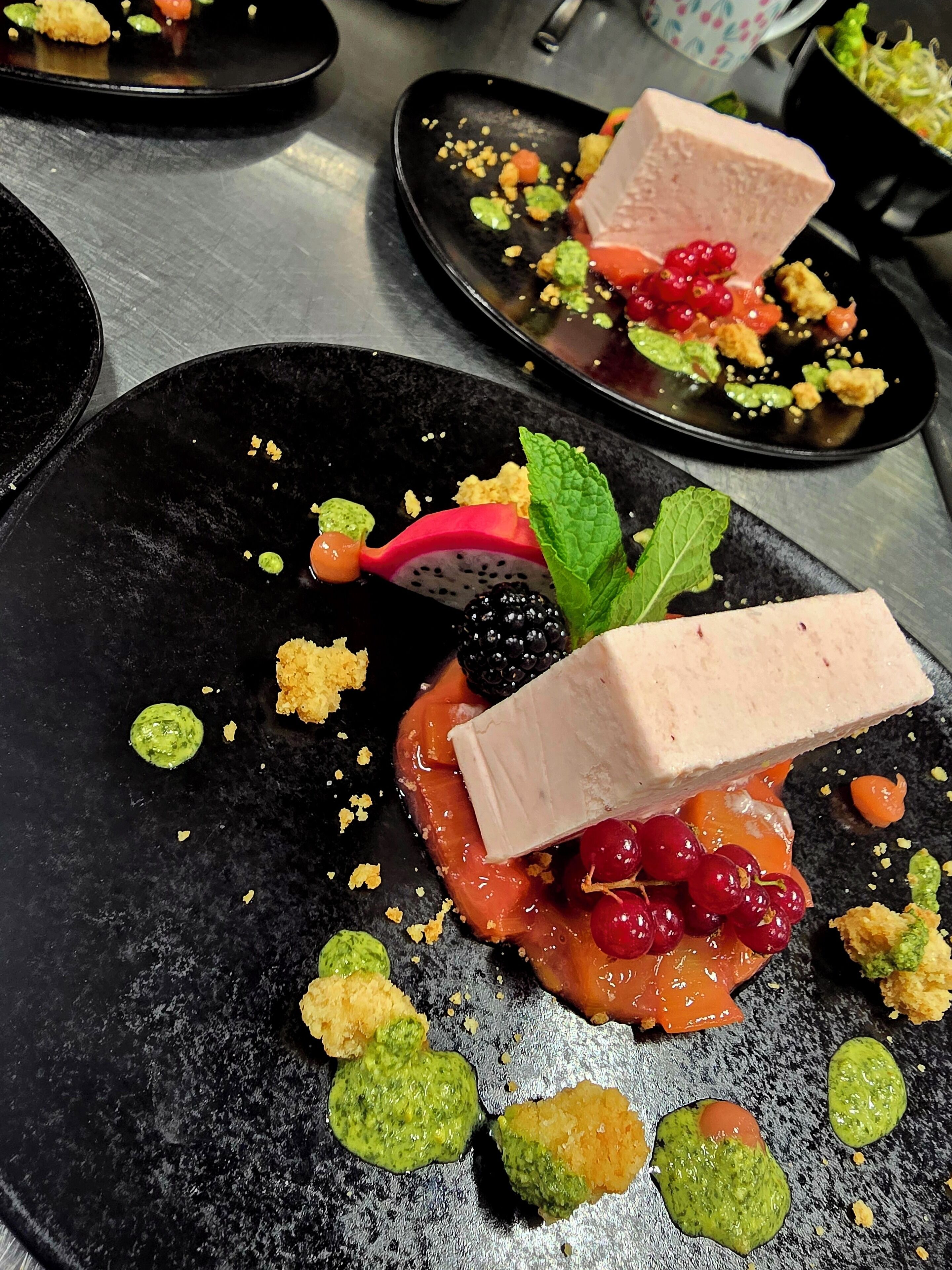 Ein Dessertteller mit Kuchenstück, Beeren und grüner Soße.