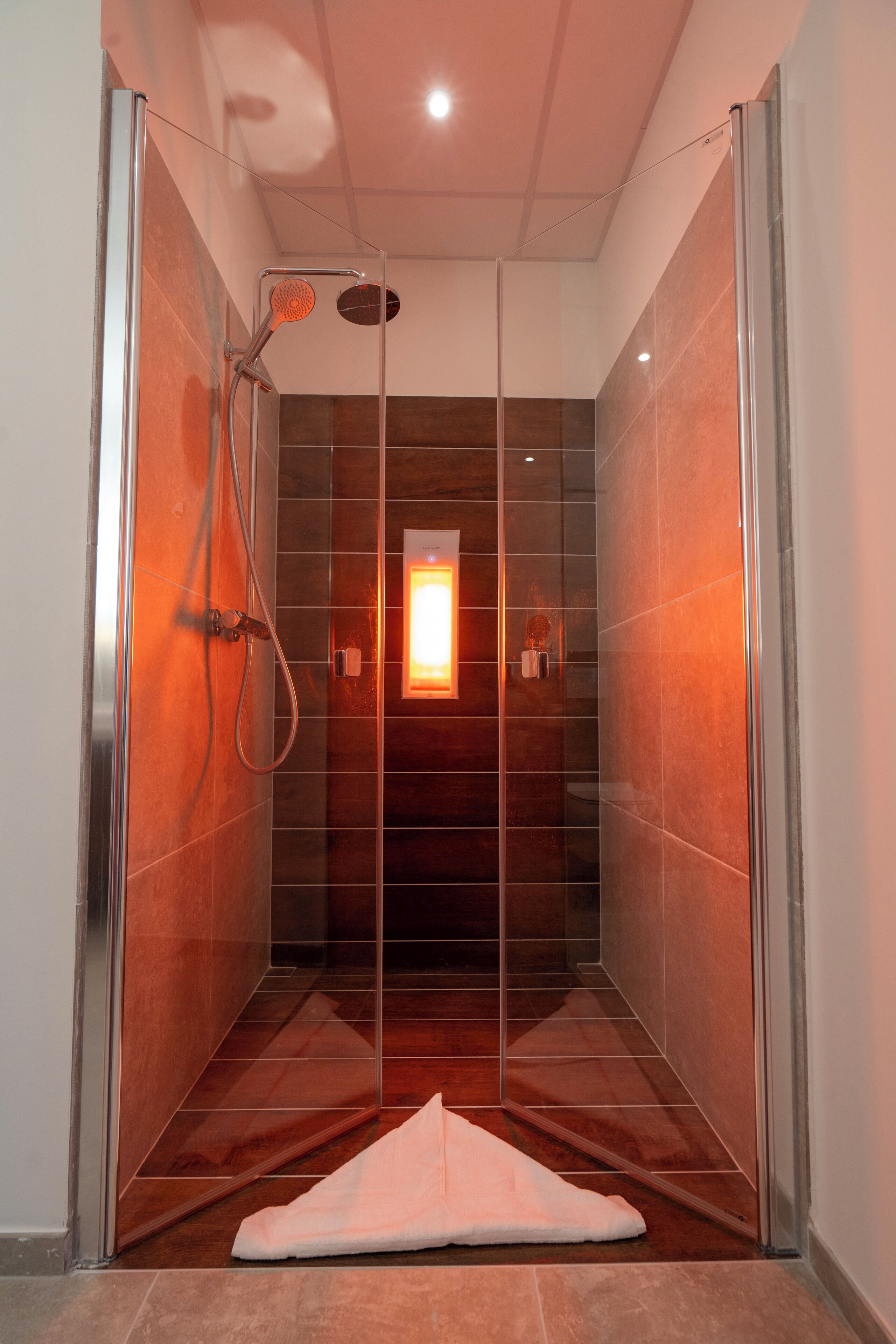 Een moderne douche met glazen deuren, een handdoek in het zicht en een klein verlicht paneel aan de wand.