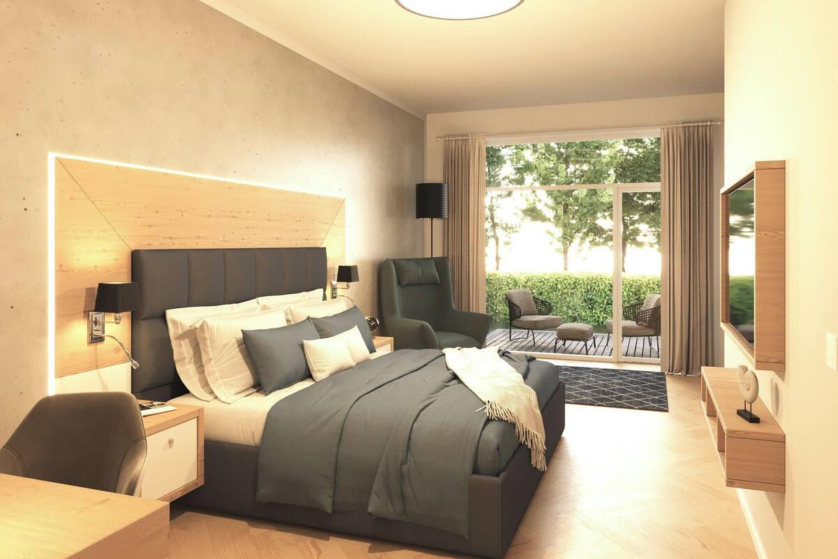A modern hotel room with a large bed, a desk, a chair, and a balcony with a view of greenery.