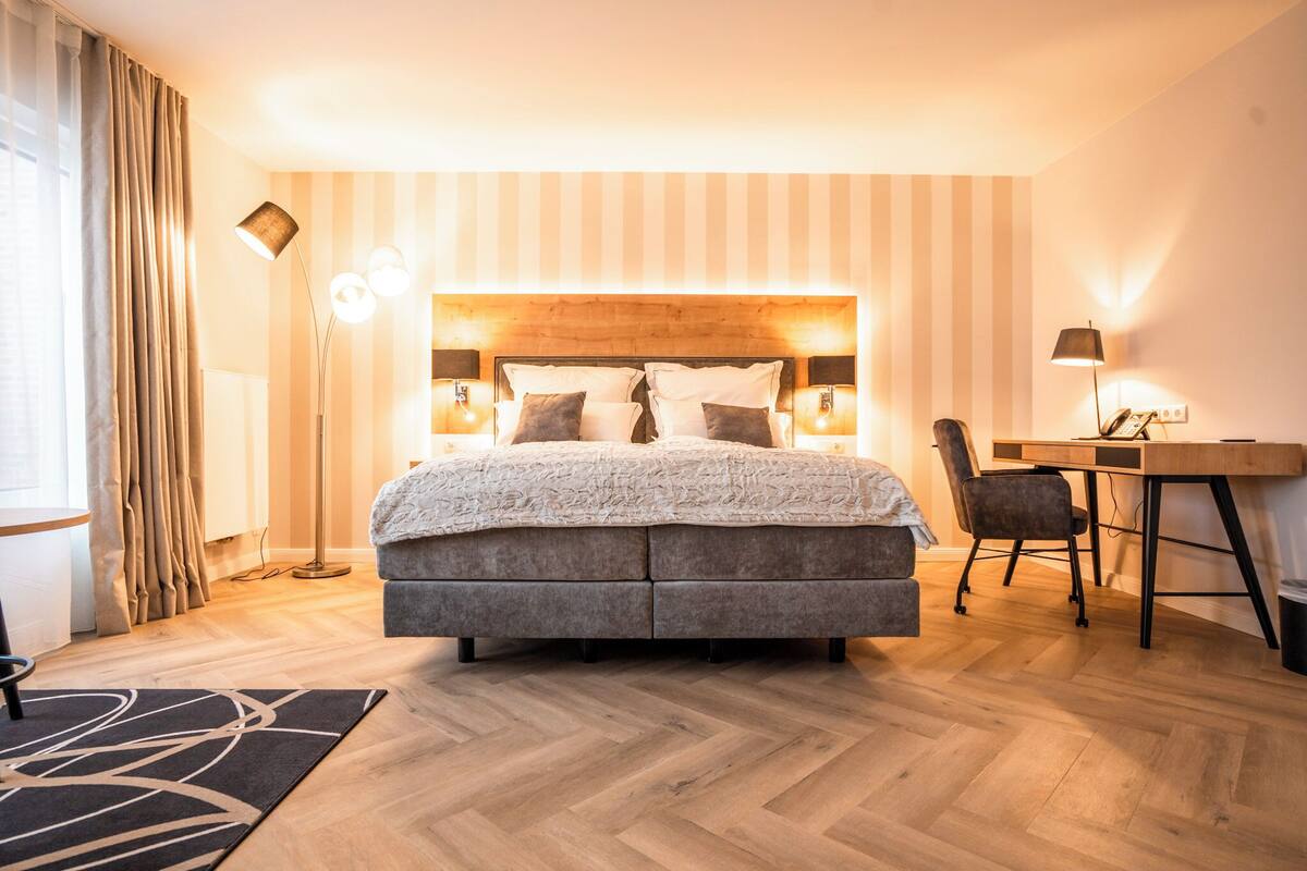 A modern hotel room with a large bed, a desk, and a chair.