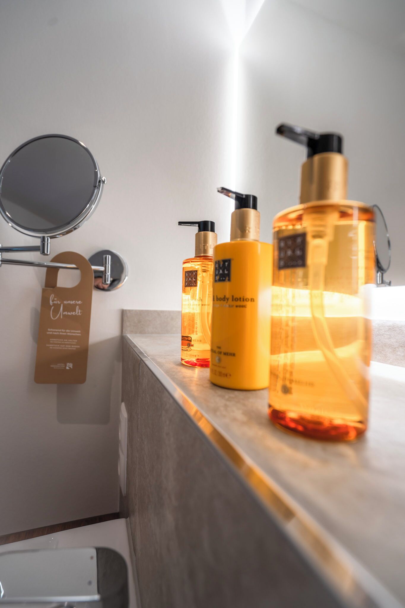 A bathroom with a mirror, a towel rack, and three bottles of body lotion on the counter.