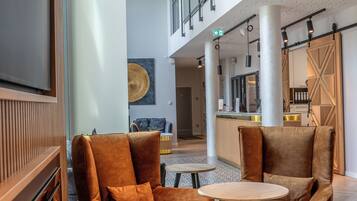 A spacious lobby with modern furniture, a large TV, and a ceiling with a perforated pattern.
