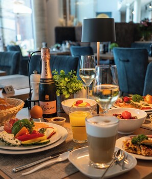 Une table à manger avec divers aliments pour le petit-déjeuner, notamment des assiettes remplies, une bouteille de champagne, des verres d’eau et de jus, et une tasse de café.