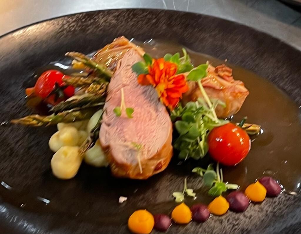 A plate with a slice of meat, vegetables, and a flower garnish.