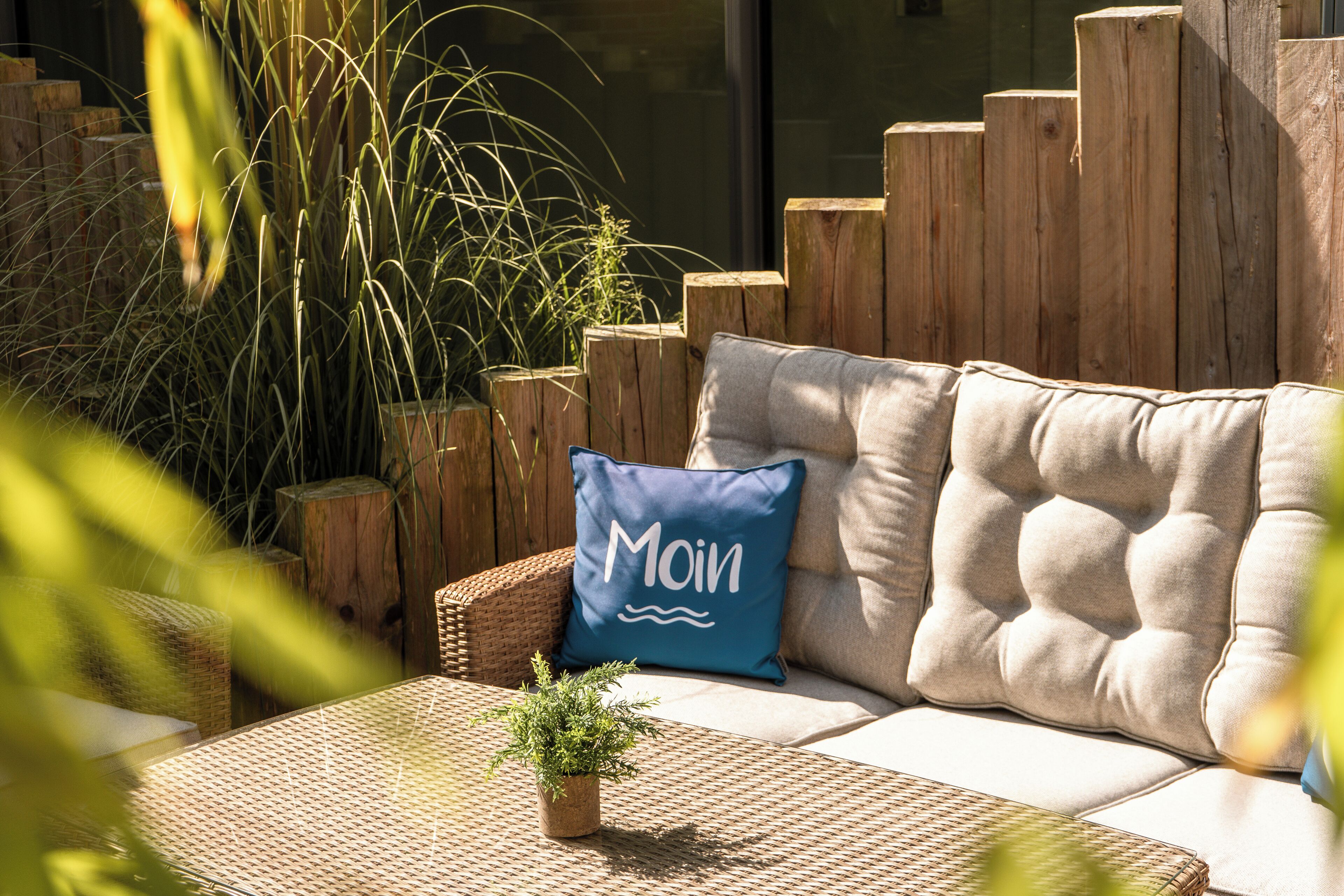 A cozy outdoor seating area with a cushioned sofa, a woven table, and a wooden fence.