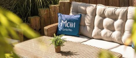 A cozy outdoor seating area with a cushioned sofa, a woven table, and a wooden fence.