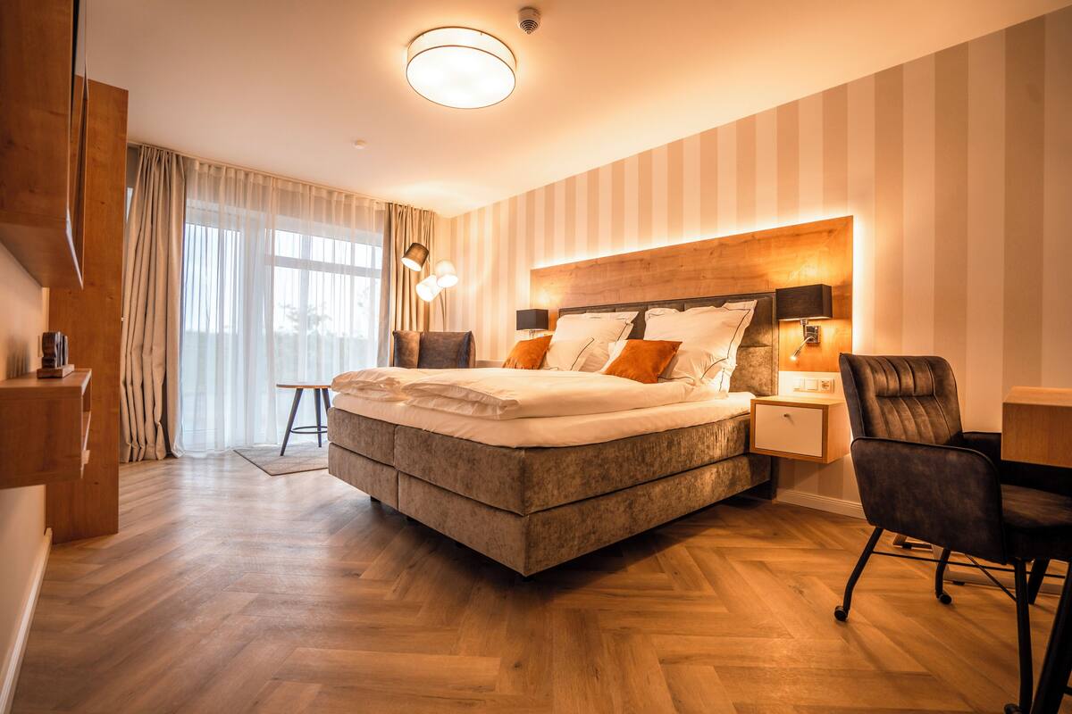 A modern bedroom with a large bed, bedside tables, a desk, and a chair.