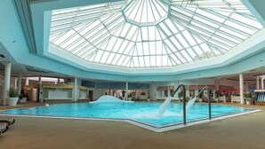 Une piscine intérieure dotée d’un toit en verre, de chaises longues et d’une cascade décorative.
