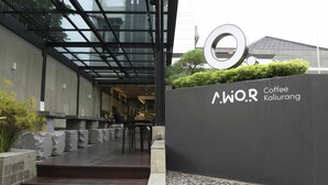 Una entrada moderna con un toldo de cristal, un letrero que dice 'Coffee Kairuang' y un camino de piedra que lleva a la entrada.