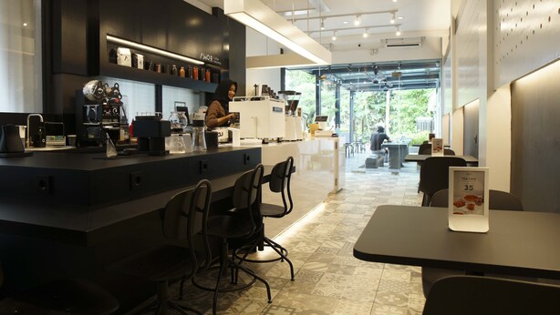 Interior moderno de una cafetería con barra, asientos y vistas al exterior.