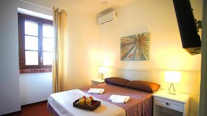 Ein Hotelzimmer mit einem Bett, zwei Nachttischen mit Lampen, einer Wandklimaanlage, einem Fenster mit Vorhängen und einem Wandbild.