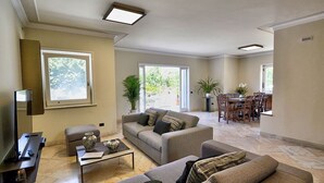 Ein geräumiges Wohnzimmer mit Sofa, Couchtisch und Fernseher, das in einen Essbereich mit Stühlen und Tisch übergeht.