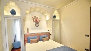 Ein Schlafzimmer mit einem großen Bett, einem Spiegel, einem Wanddekor und einem kleinen Tisch mit einer Vase.